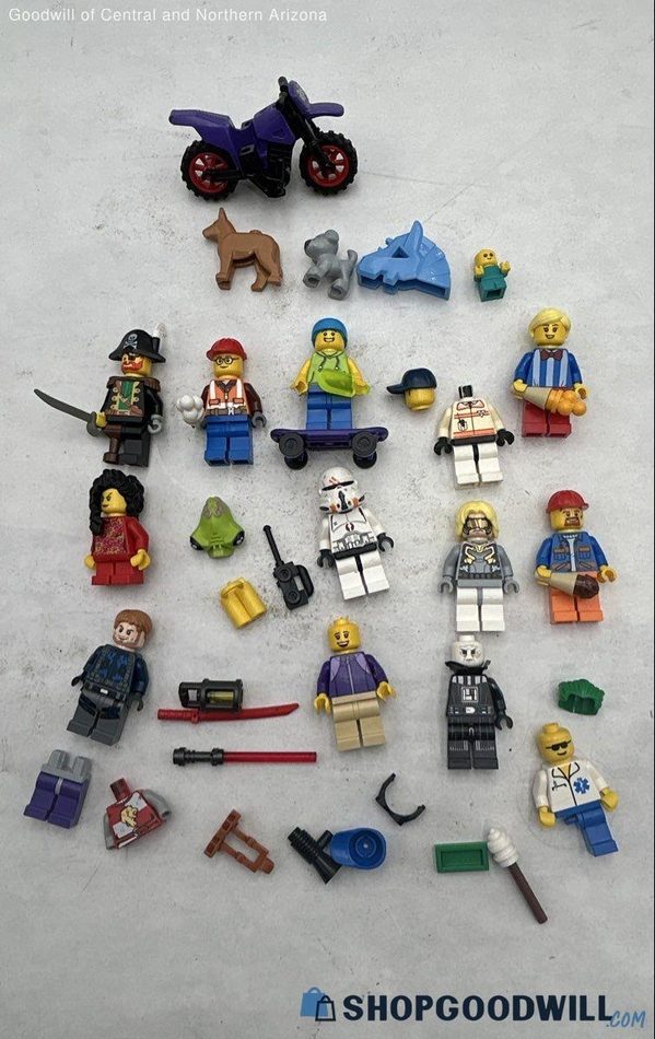 A ShopGoodwill lot photo of LEGO minifigures broken apart — loose heads, torsos, legs, hairpieces, weapons, and accessories scattered, with several figures clearly incomplete